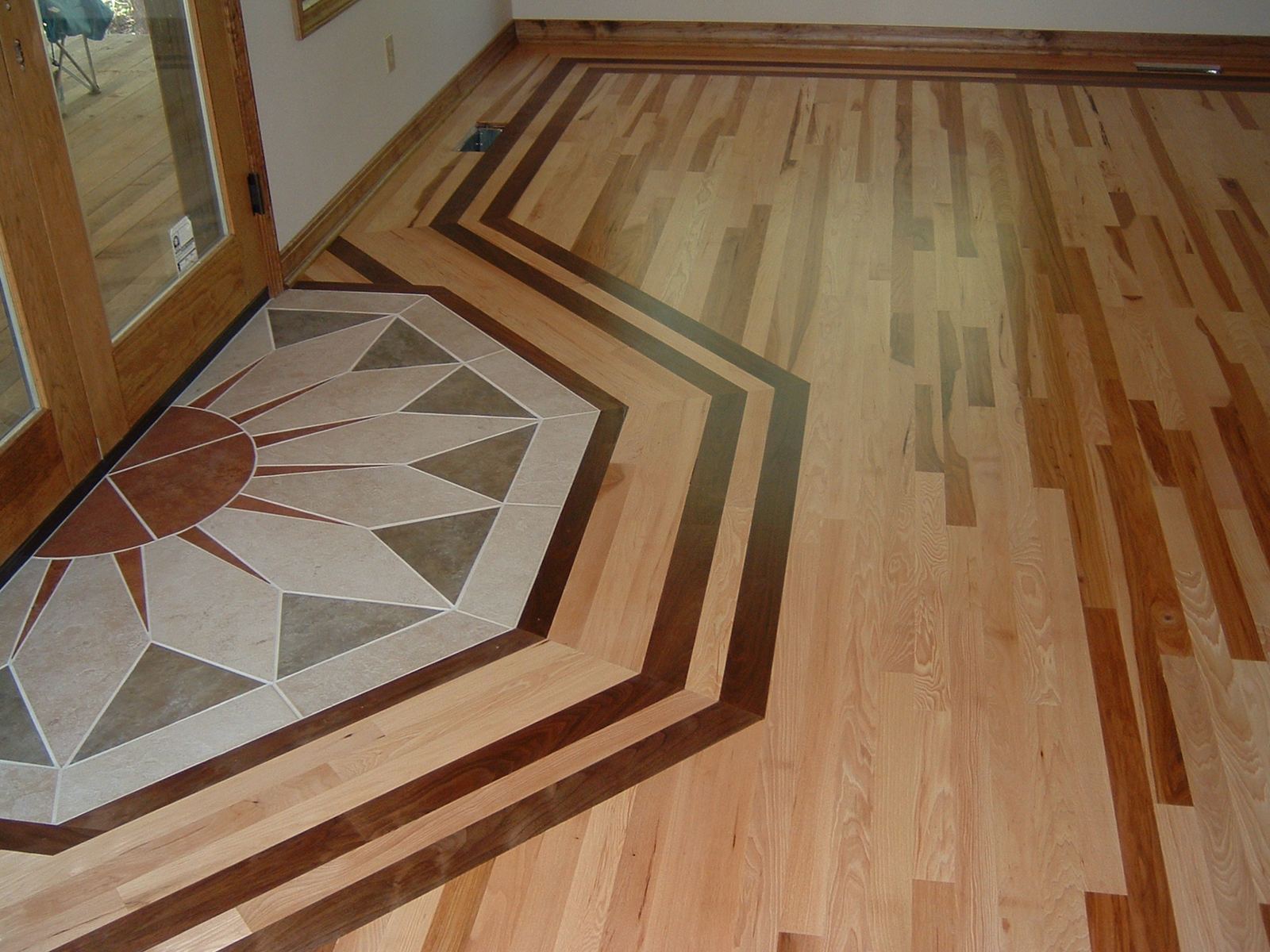 Light hickory floor with dark walnut border strips framing a tile medallion at the entry