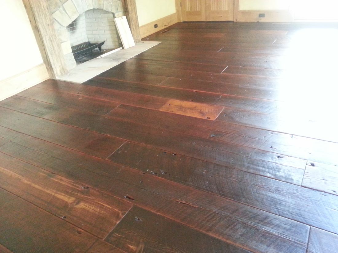 Dark reclaimed 12 inch heart pine planks in front of a stone fireplace