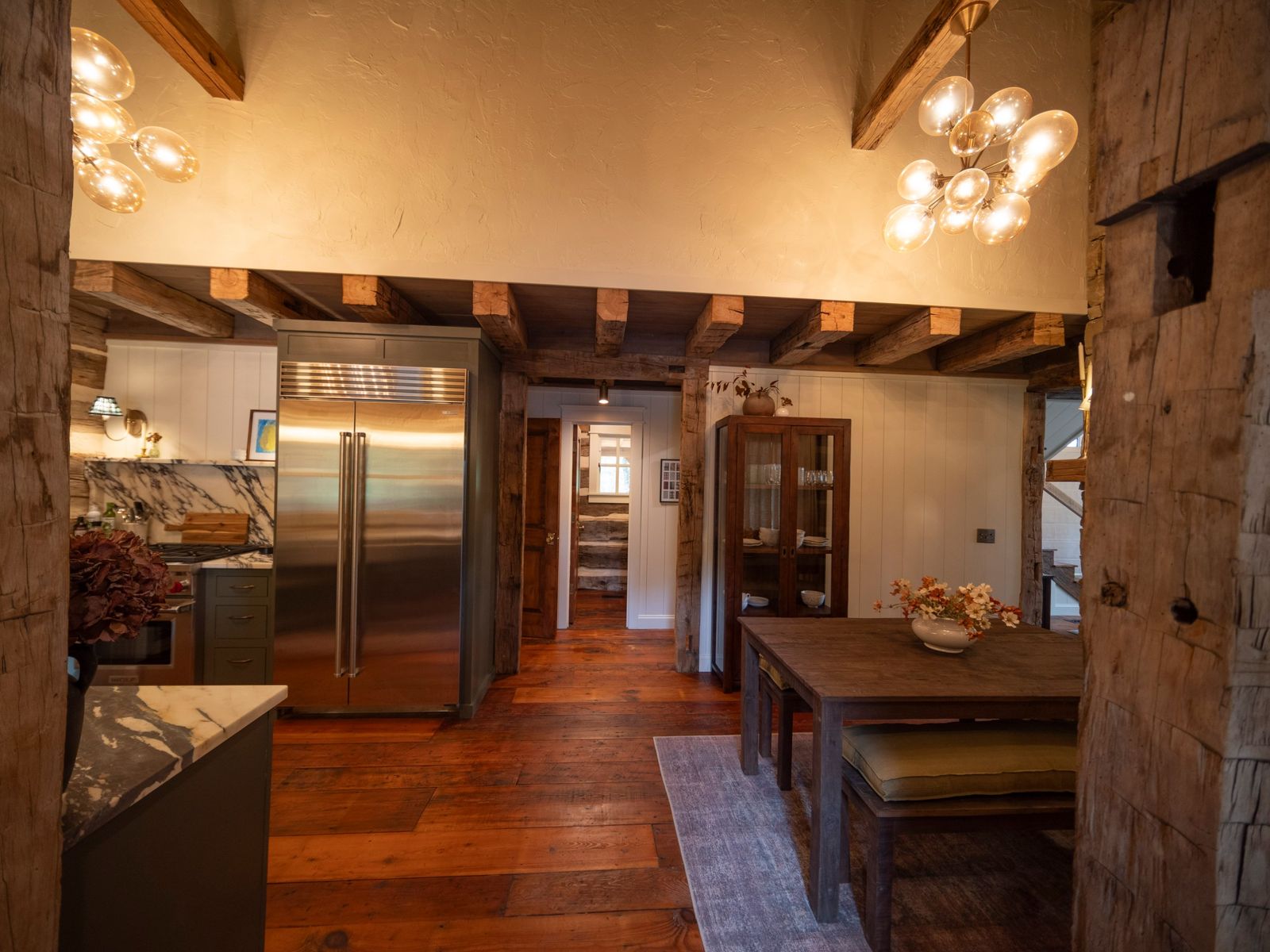 Wide reclaimed pine plank floor running through a kitchen and dining room with hand-hewn beams and posts