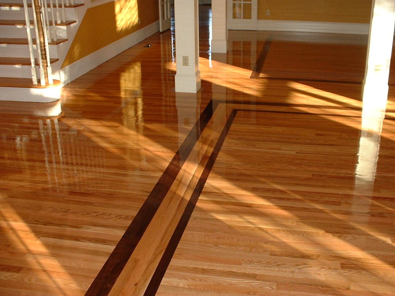 Glossy red oak floor with a dark walnut border running through a sunlit entry