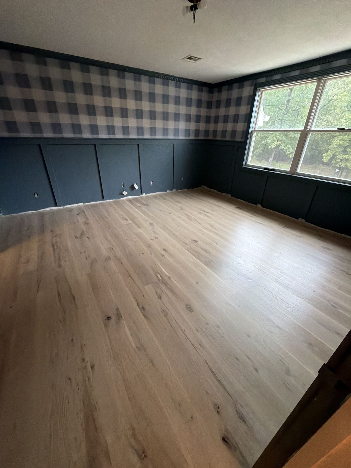 Newly finished white oak floor with a natural, raw-wood look in a bedroom with navy wainscoting